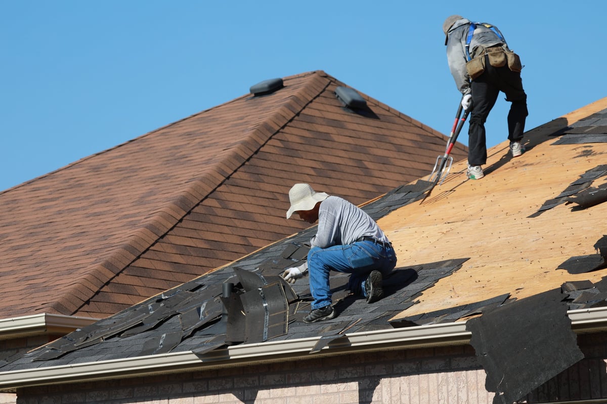 Roofers removing old asphalt shingles from a residential roof during a full replacement