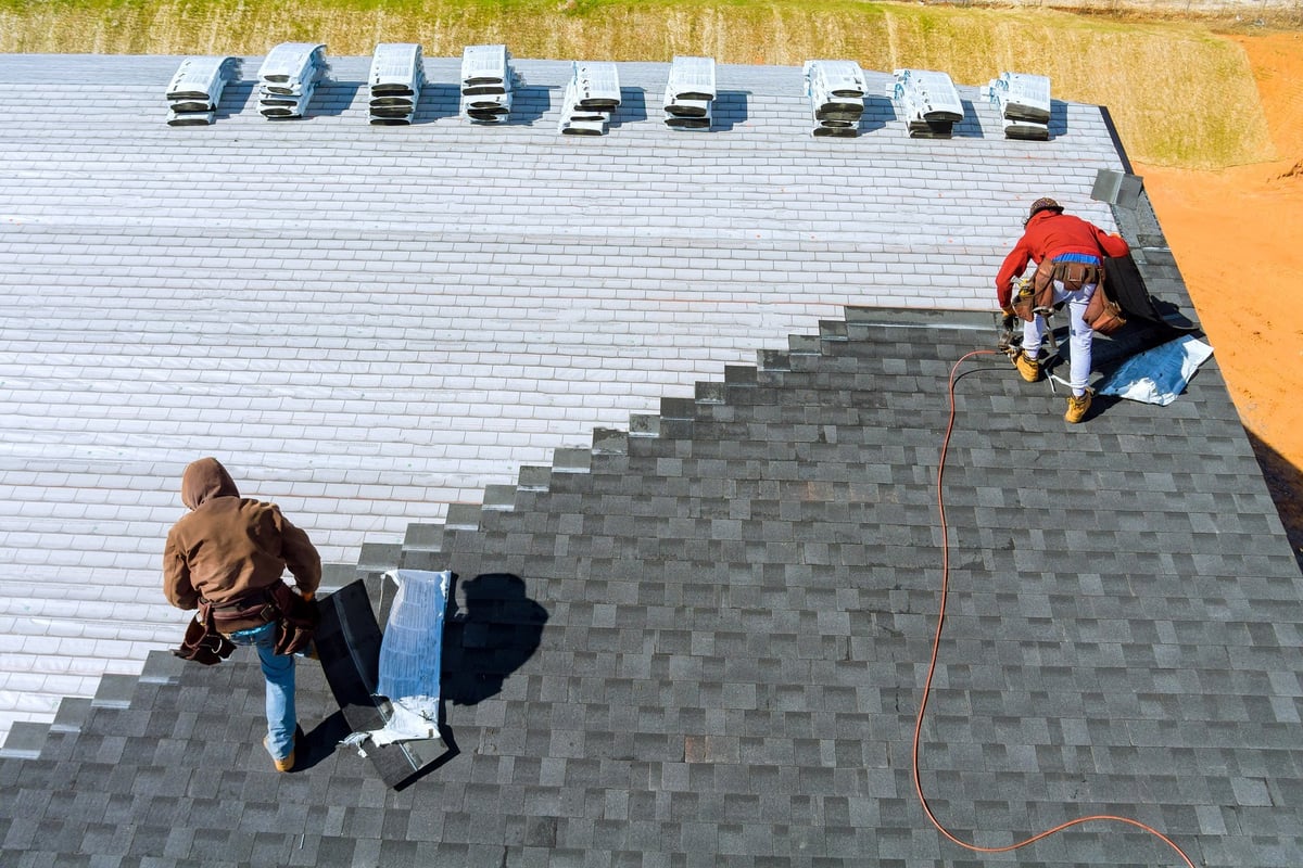 Worker installing roof shingles with an air hammer and nail