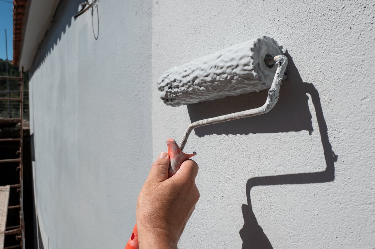 Painter's hand using a roller to apply paint to an exterior wall