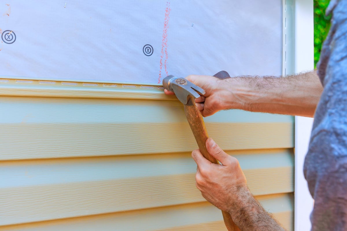 Worker using a hammer to secure new siding during a home exterior renovation