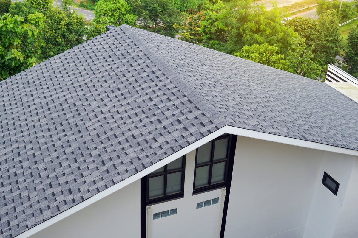 Newly installed gray asphalt shingle roof on a modern home surrounded by green trees