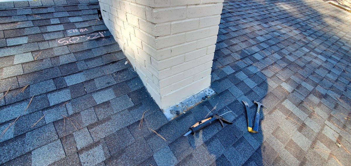 Brick chimney with a protective metal cap and counter-flashing meeting an asphalt shingle roof