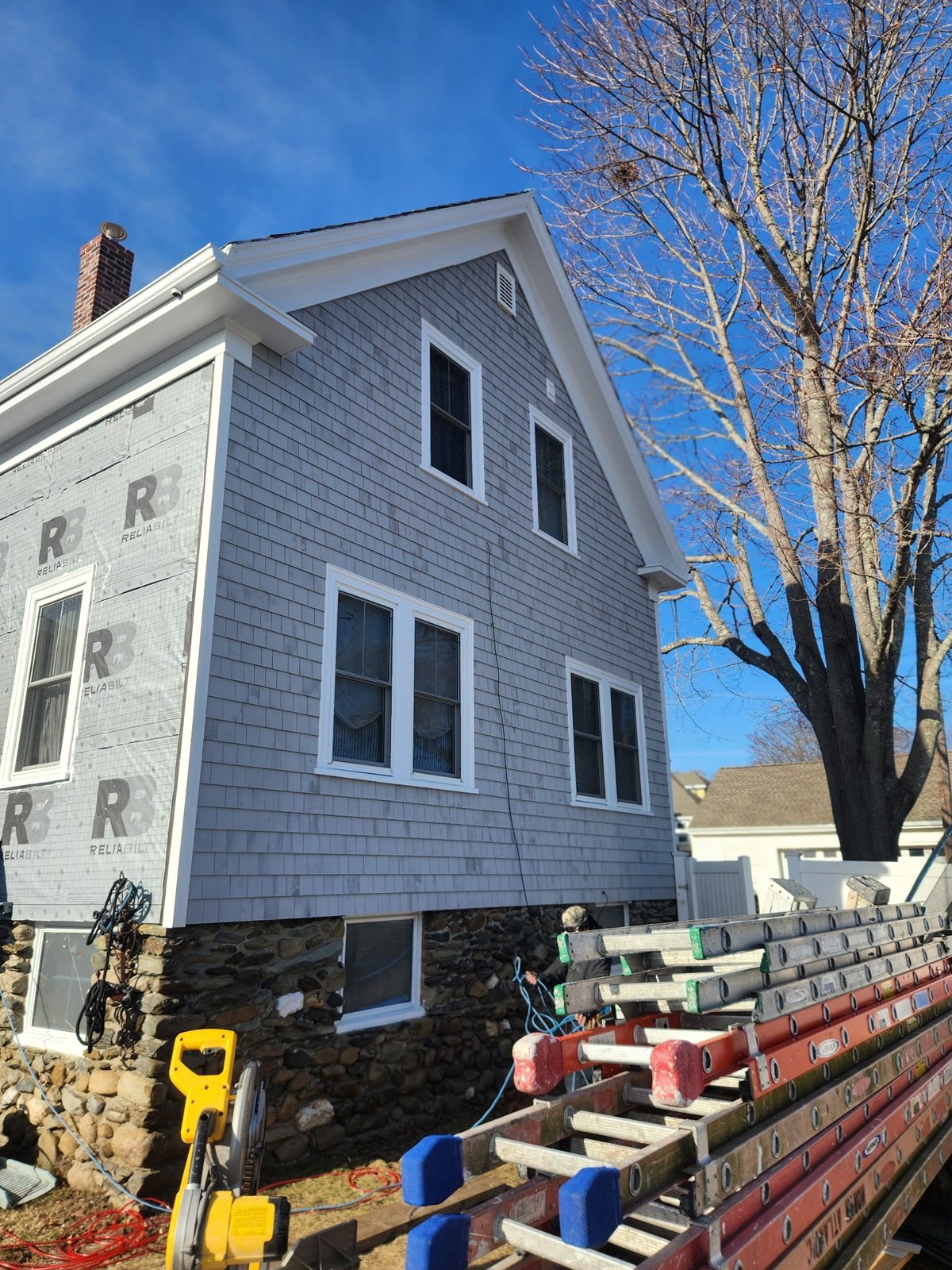 Two-story blue house under construction with exposed foundation and construction equipment.